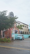 A pastel-colored building features a sign for Archie's of Siesta Key and appears to house a massage therapy business. A light blue Mini Cooper is parked in front of the building. The scene includes palm trees and a wet road, suggesting recent rain.