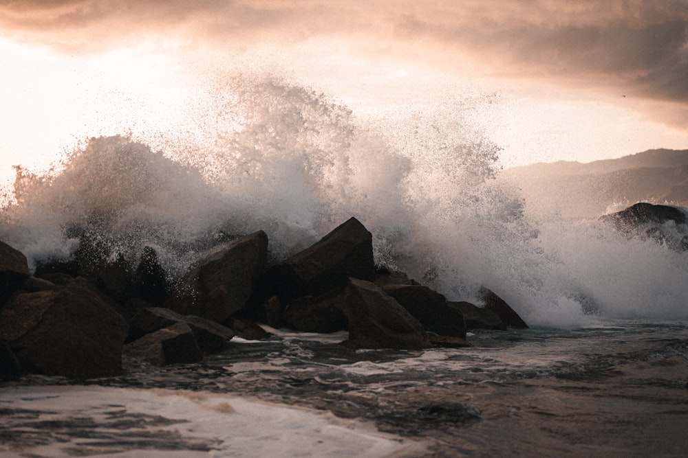 a large wave crashing over rocks on a beach