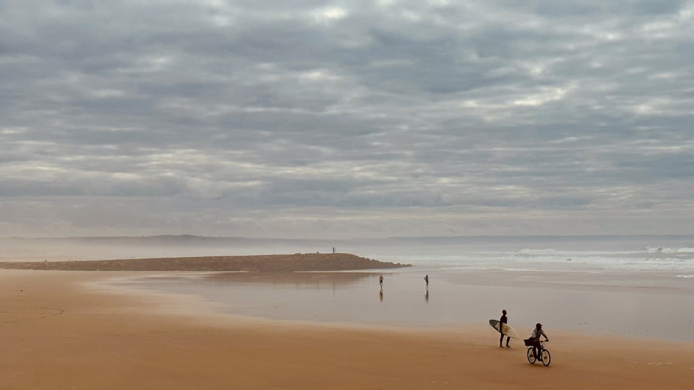 a couple of people riding bikes on top of a sandy beach