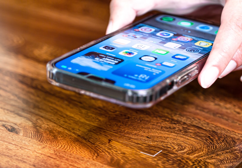 a person holding a cell phone on top of a wooden table