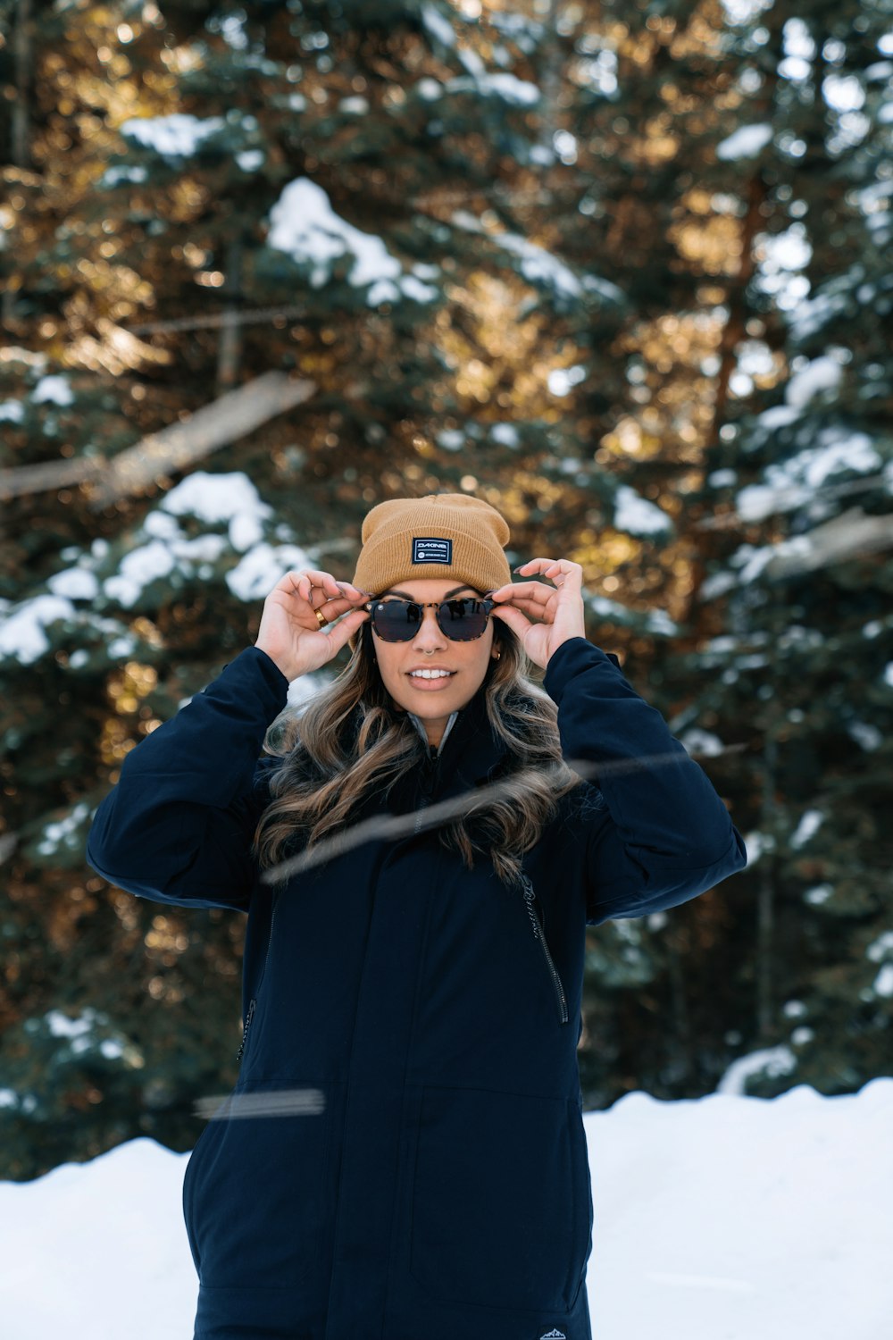 a woman wearing a hat and sunglasses standing in the snow