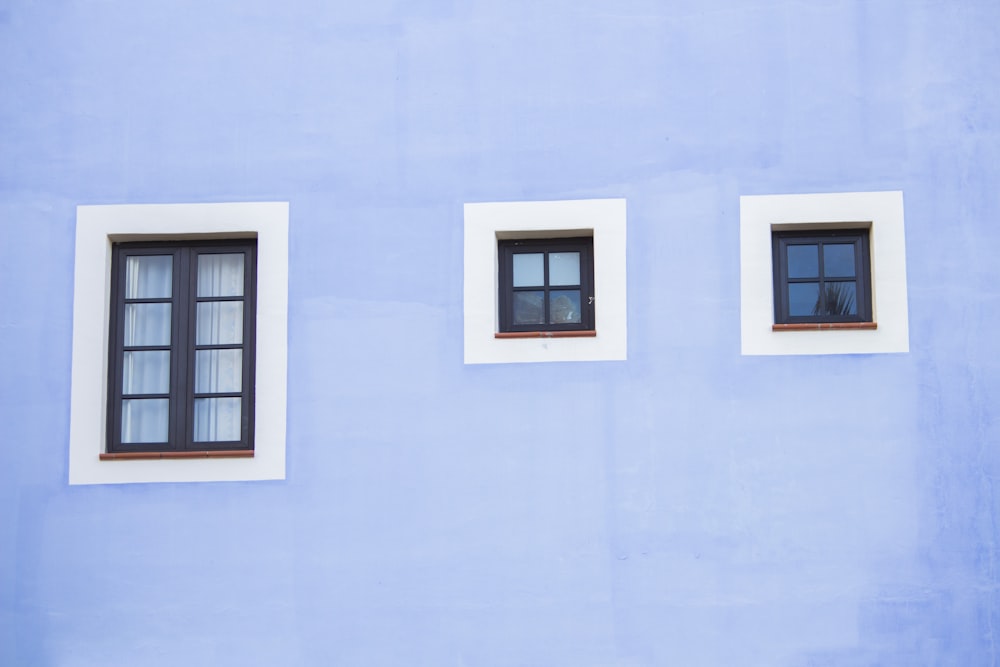 three windows on the side of a blue building