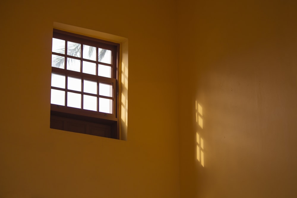 a window in a yellow wall with the sun shining through