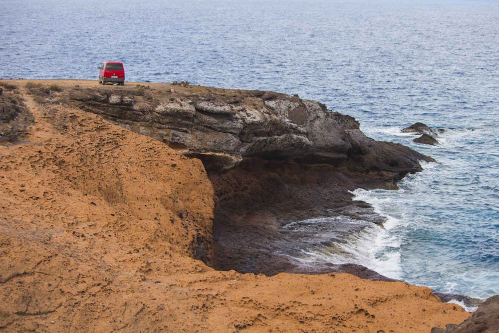 a red truck driving down a cliff by the ocean