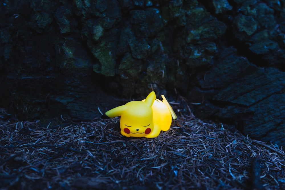 a pikachu figurine sitting on the ground next to a tree