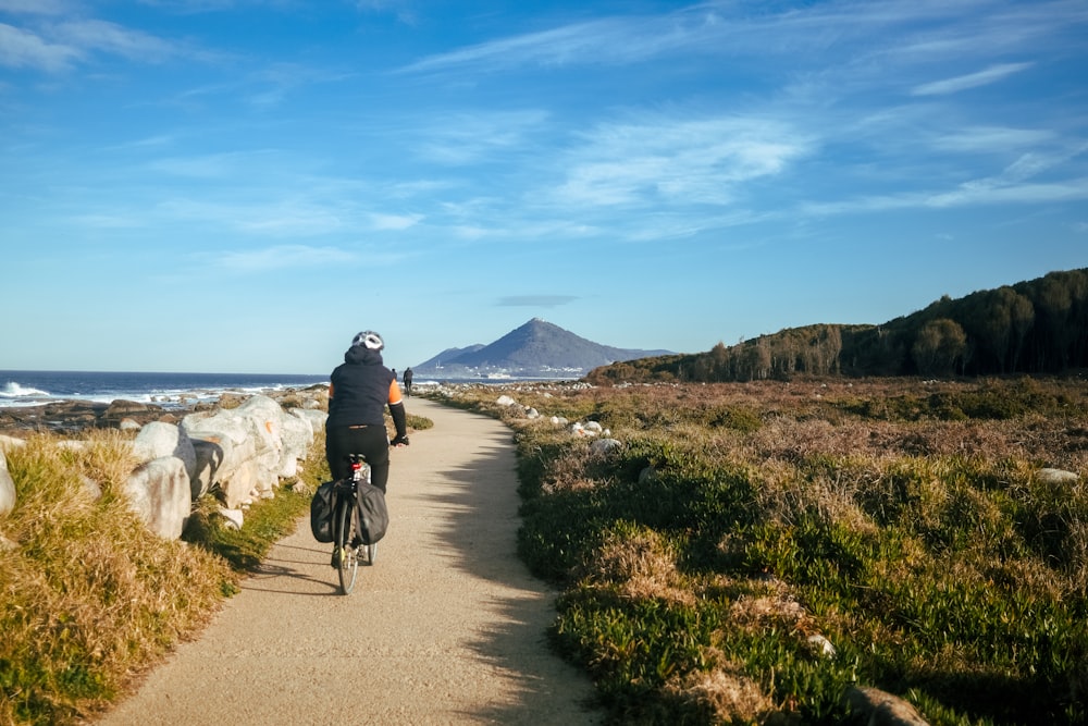 a man riding a bike down a dirt road next to the ocean