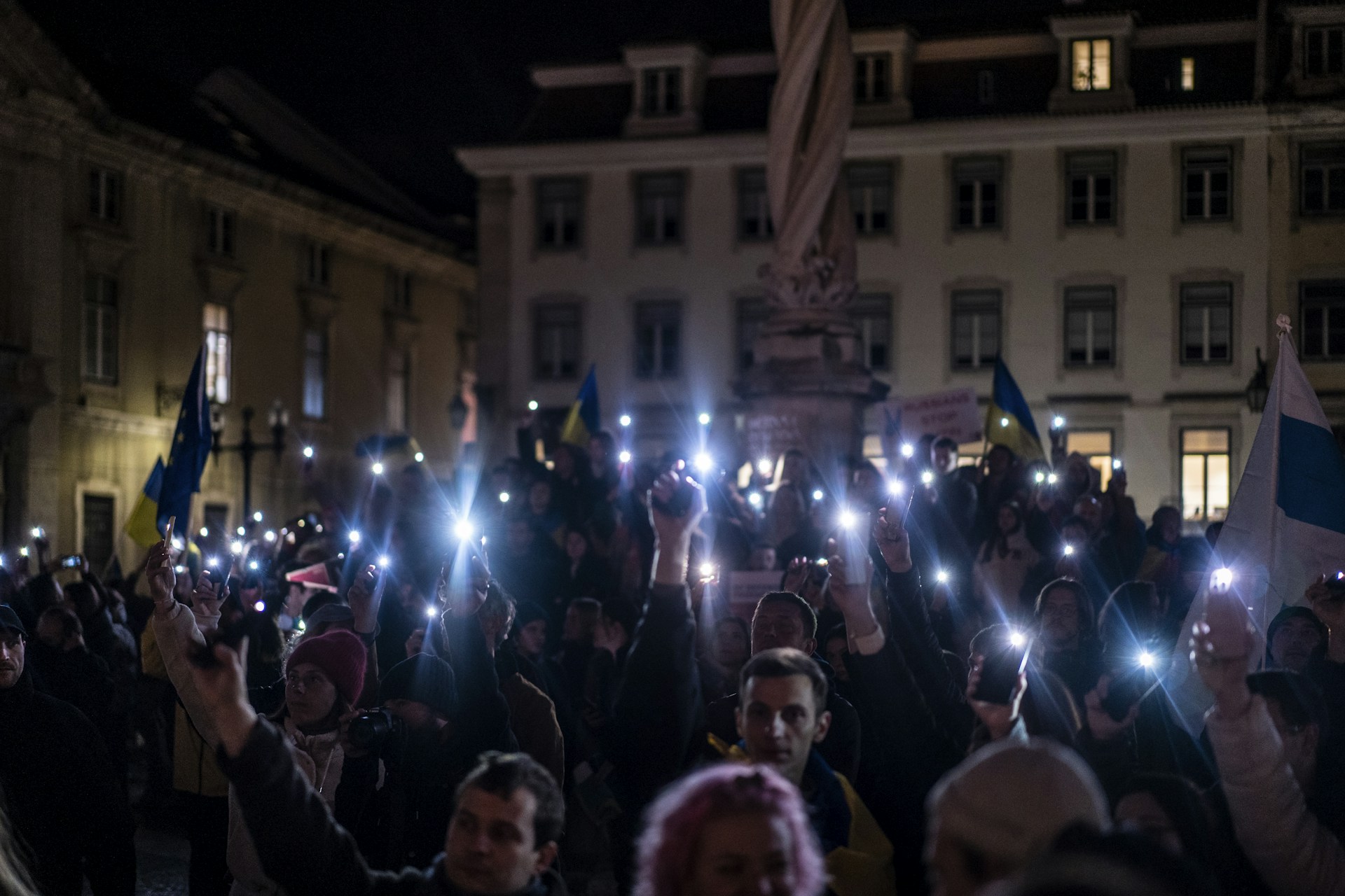 Nighttime image showing a line of people holding candles and phones lighting the square, symbolizing hope and solidarity after a day of protests.