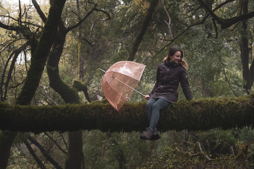 a woman sitting on a tree branch holding an umbrella