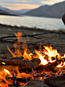A cozy campfire glowing warmly under a star-studded sky beside a flowing river.