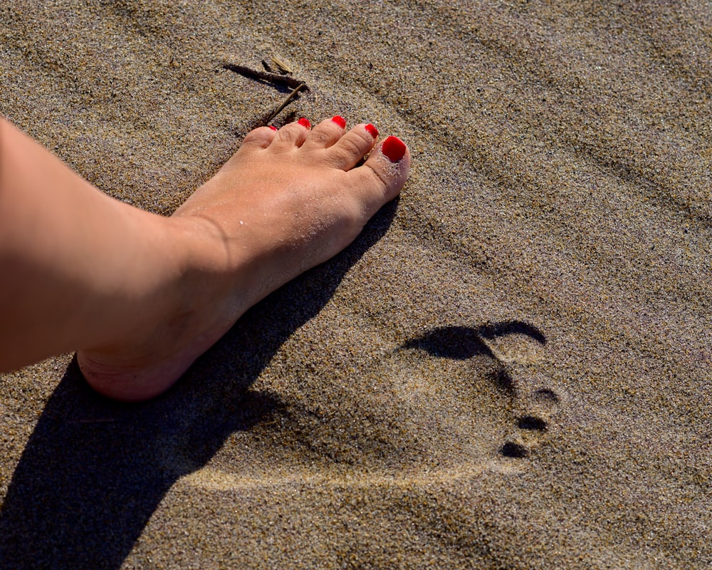 El pie descalzo de una mujer y el esmalte de uñas rojo en una playa de arena