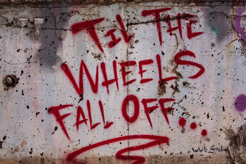 graffiti on the side of a building reads, let the wheels fall off