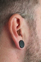 A close-up of a person's ear with a stretched piercing, featuring a black plug.