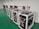 Several battery storage systems are organized in a room with a green floor. Each system is housed within a white metal frame, featuring black components and various wiring connections. Coiled cables hang on the wall, and some cables are on the floor in front of the systems.