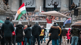 A Kurdish activist passionately speaking at a protest rally, surrounded by supporters holding banners.