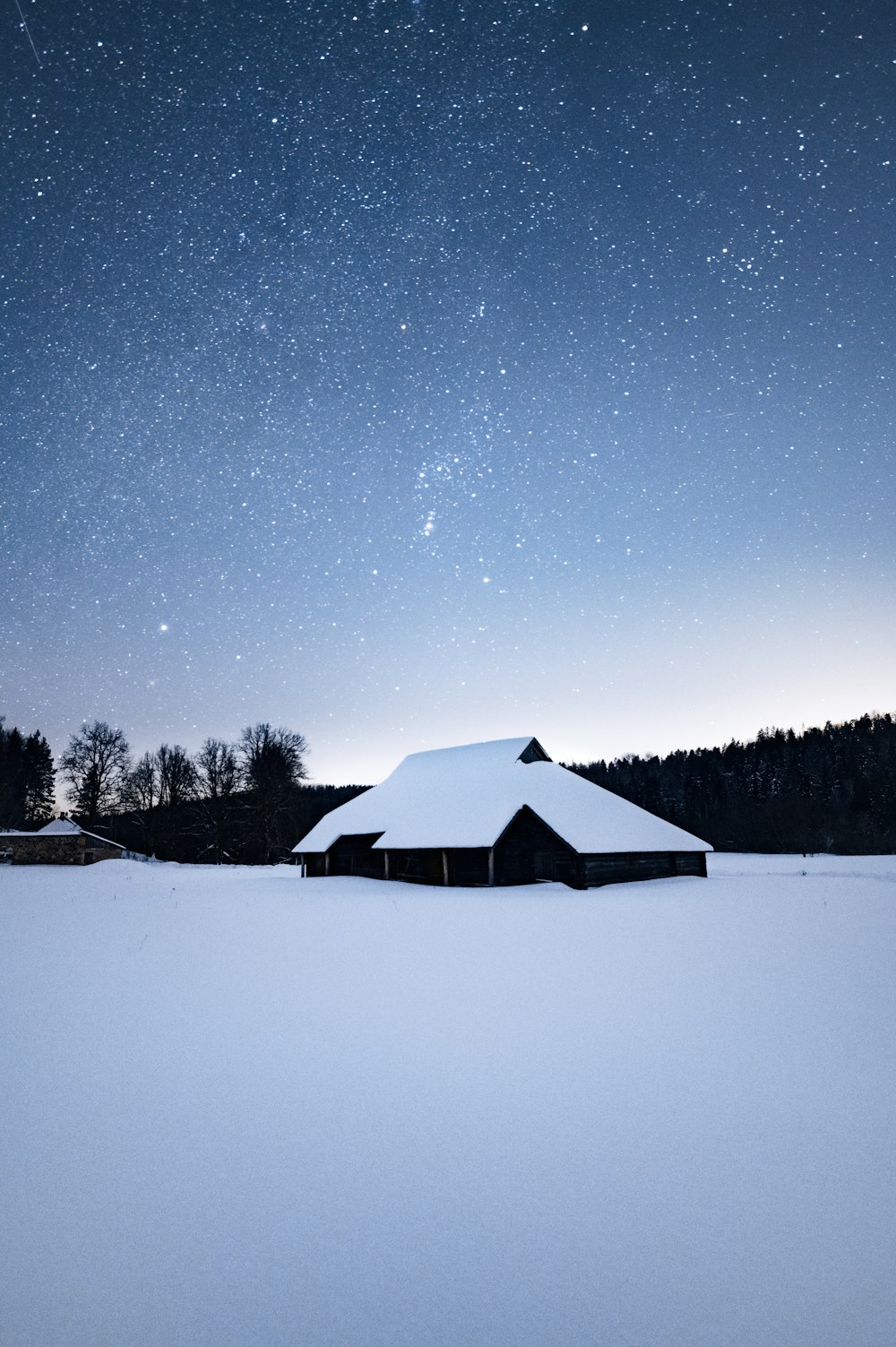 a barn in a snowy field under a night sky