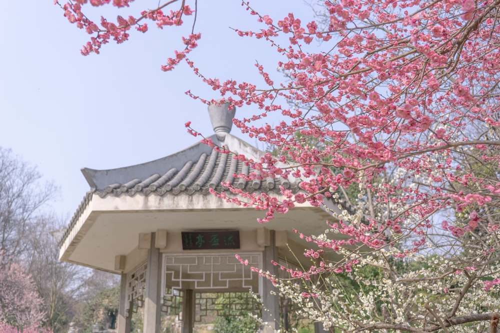 a gazebo with a clock in the center surrounded by pink flowers