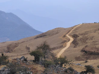 Dirt path winding through raw land with distant hills.