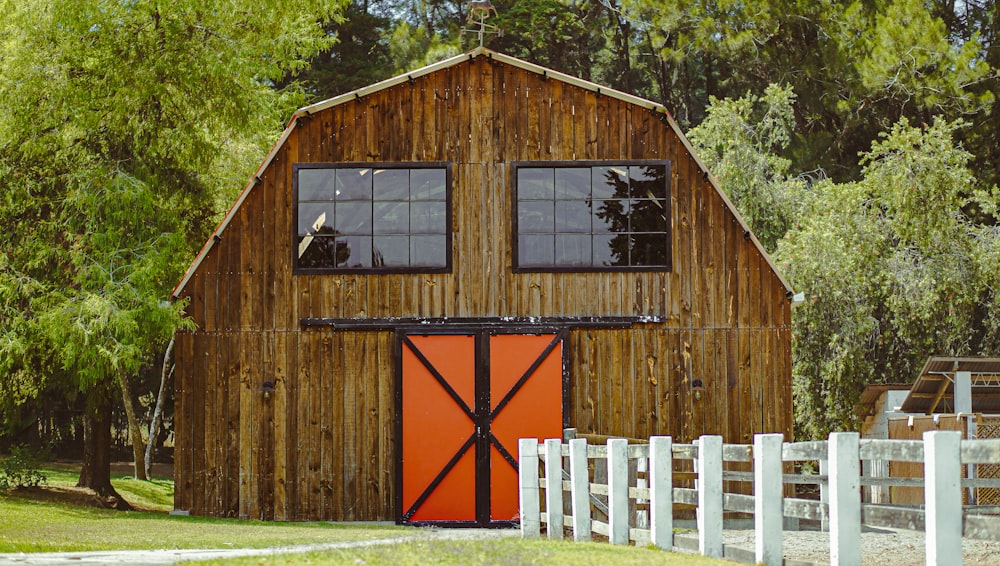 a barn with a red door and a white fence