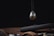 A spherical, futuristic device with a glossy black and silver finish, partially suspended. It has yellow accents and numbers, resembling a timer or measuring tool. Beneath it, a wooden surface holds a brown leather strap and dark metallic objects, suggesting a high-tech or mechanical setting.