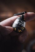 A close-up of a hand holding a small, round device with a black and yellow design. The device features numbers, possibly indicating some form of measurement or countdown, and a strap attached to its top.