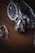 A high-quality wristwatch with a metallic chain bracelet is paired with an intricate, modern-looking keychain that resembles a mechanical object. These items are set against a dark wooden surface, providing a rich contrast to the polished metal of the watch and keychain.