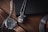 A luxurious wristwatch with a brown leather strap and a detailed face is placed on a wooden surface. Next to it, a metallic ball pendant with a snake design wraps around it. Both items are situated near a dark-colored notebook and part of a metal object, possibly a cup or plate.