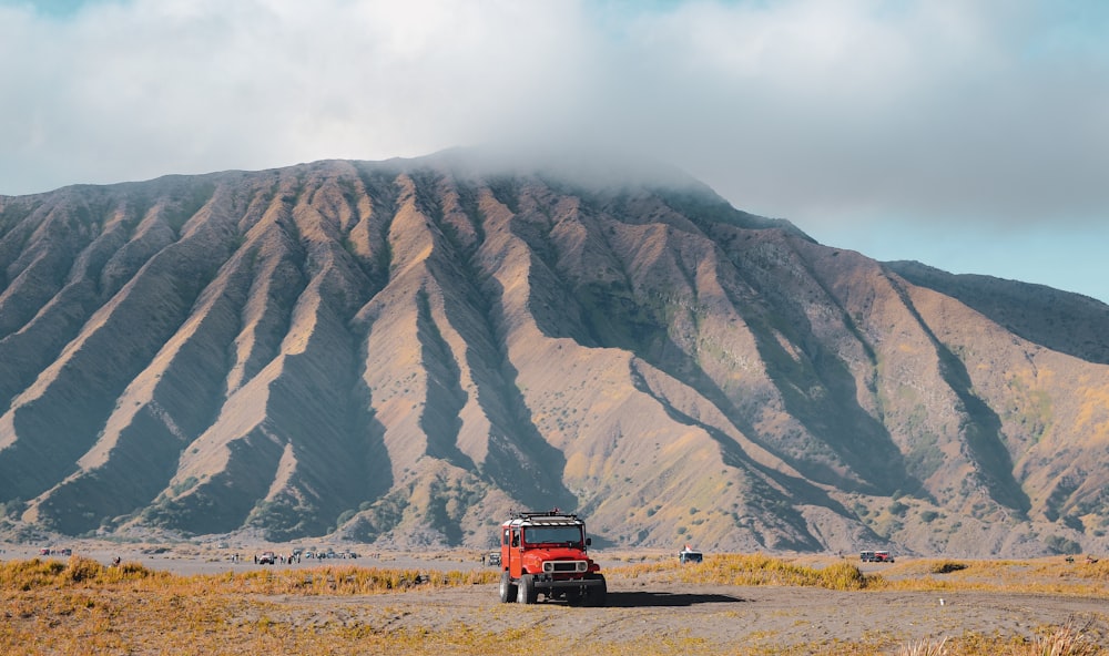 a red truck driving down a dirt road next to a mountain