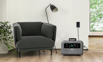 A compact home backup battery unit neatly placed in a cozy living room corner with plants nearby.
