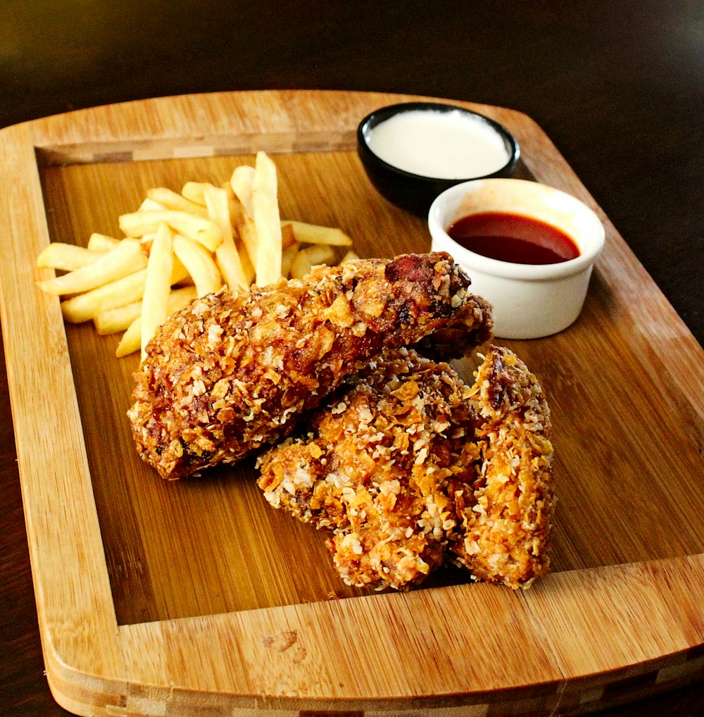 a wooden tray topped with fried chicken and french fries