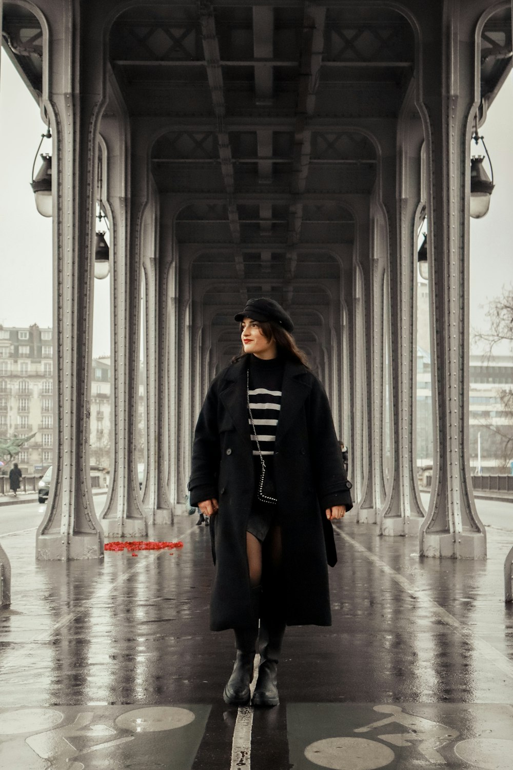 a woman in a black coat is standing under a bridge