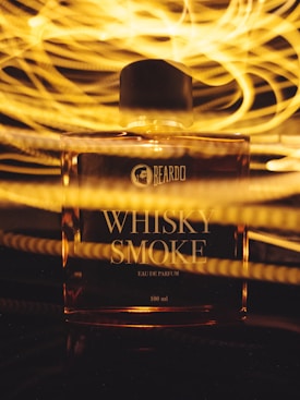 A perfume bottle labeled 'WHISKY SMOKE' is illuminated with warm, swirling golden lights in the background, creating an artistic and vibrant effect.