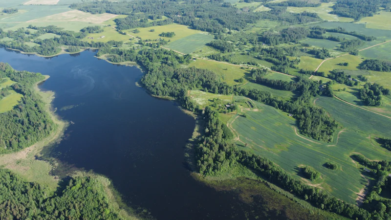 Aerial view of a calm lake surrounded by green fields and forest in Latvia