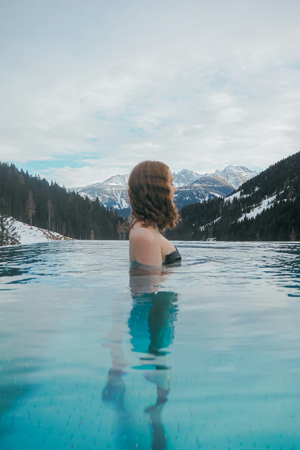 Une femme assise dans une piscine d’eau avec des montagnes en arrière-plan