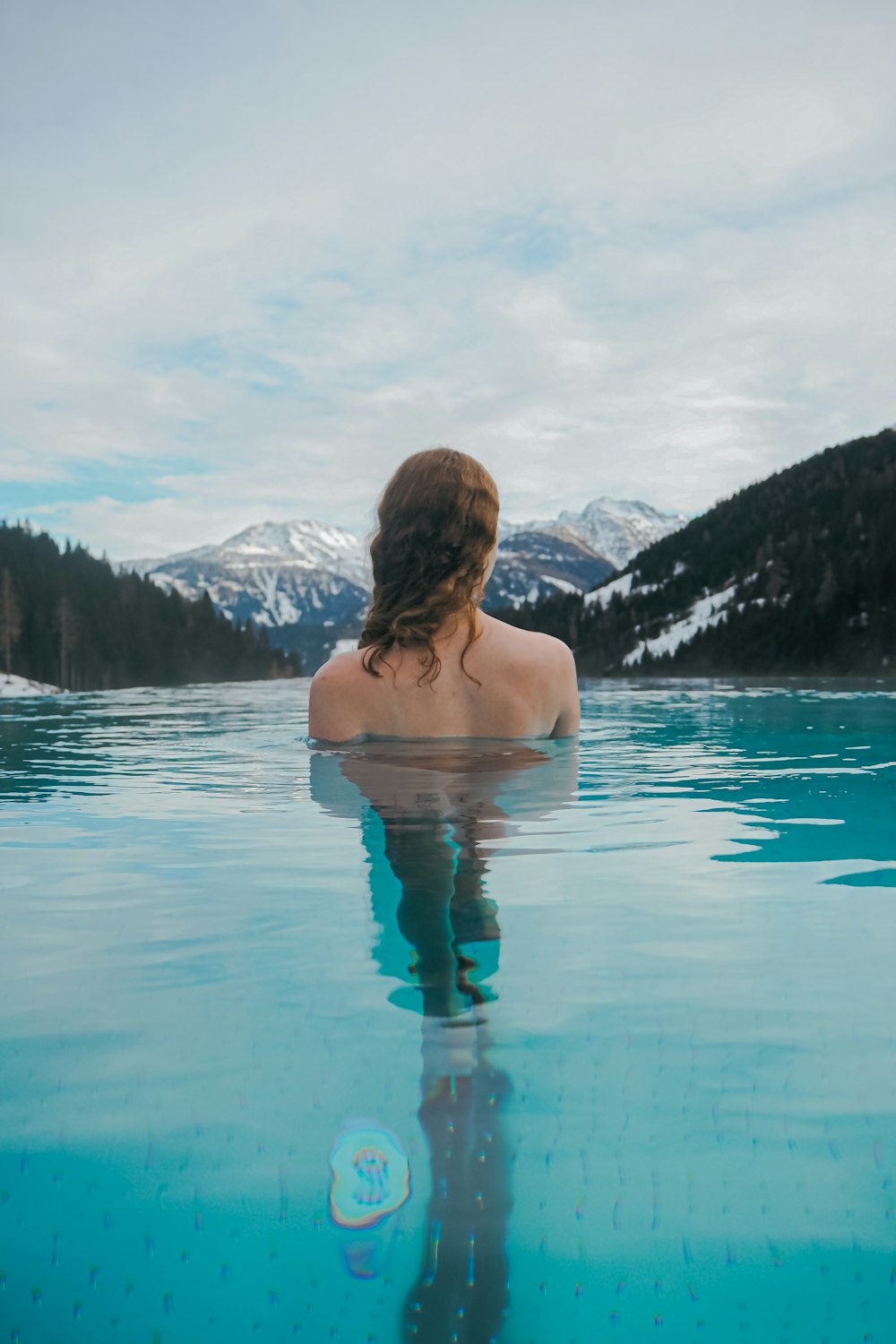 Une femme assise dans une piscine d’eau avec des montagnes en arrière-plan