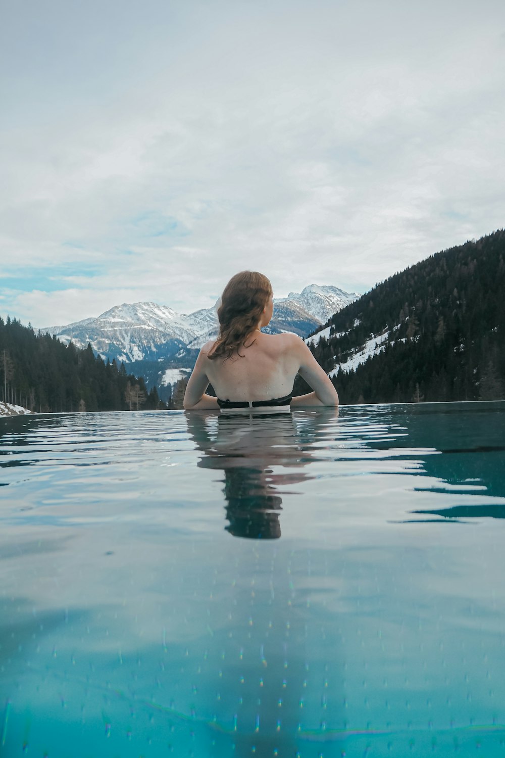 a woman sitting in a pool of water with mountains in the background