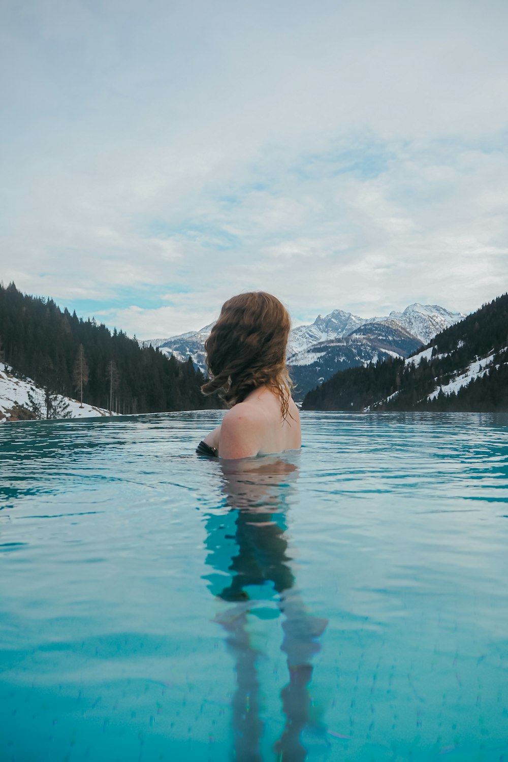 a woman sitting in a pool of water with mountains in the background