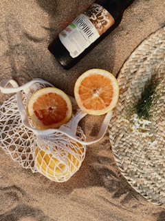 a bottle of booze next to two grapefruits on a beach