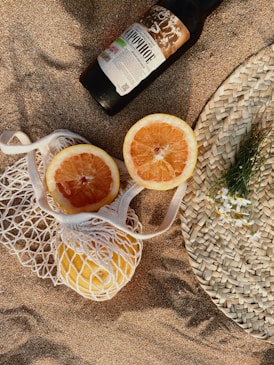 a bottle of booze next to two grapefruits on a beach
