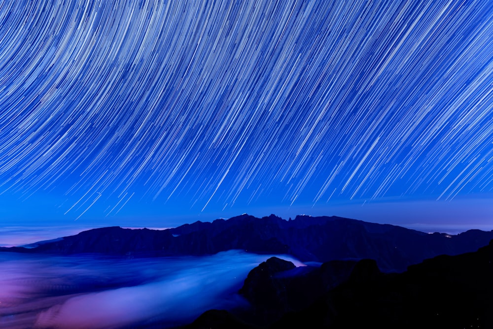 the night sky with a star trail over a mountain range