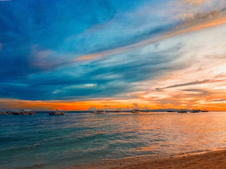 A vibrant sunset over the iconic Arch of Cabo San Lucas with colorful boats in the foreground.