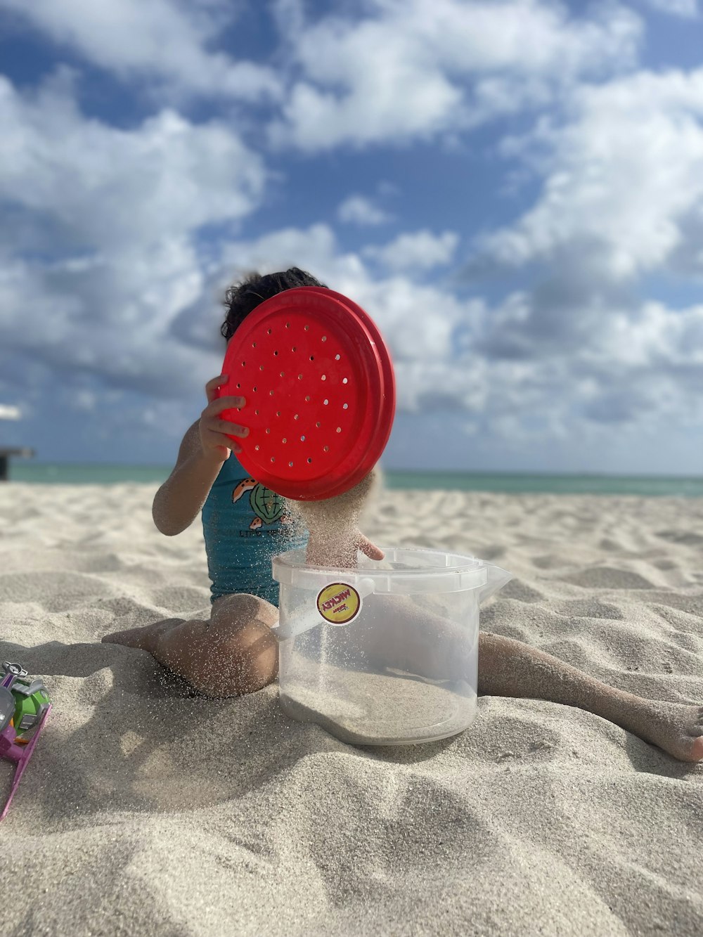 a little girl sitting in the sand with a frisbee