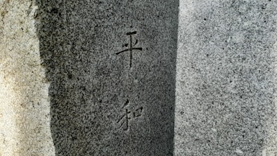 A close-up view of a granite stone surface with engraved Chinese or Japanese characters. The stone appears textured and has variations in light and shadow, giving it a three-dimensional feel.