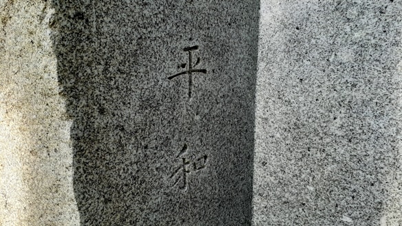 A close-up view of a granite stone surface with engraved Chinese or Japanese characters. The stone appears textured and has variations in light and shadow, giving it a three-dimensional feel.