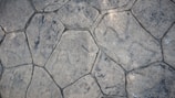 A textured surface composed of irregularly shaped stone tiles, each tile defined by distinct edges and a slightly weathered appearance. The stones vary in size and pattern, showing subtle variations in color and surface detail.