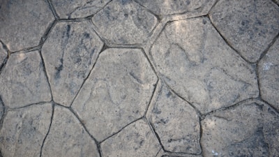 A textured surface composed of irregularly shaped stone tiles, each tile defined by distinct edges and a slightly weathered appearance. The stones vary in size and pattern, showing subtle variations in color and surface detail.