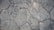 A textured surface composed of irregularly shaped stone tiles, each tile defined by distinct edges and a slightly weathered appearance. The stones vary in size and pattern, showing subtle variations in color and surface detail.