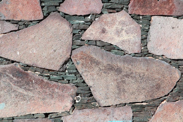 Large irregular stone slabs of various sizes are meticulously arranged with dark mortar visible in between, forming a rustic and textured pattern.
