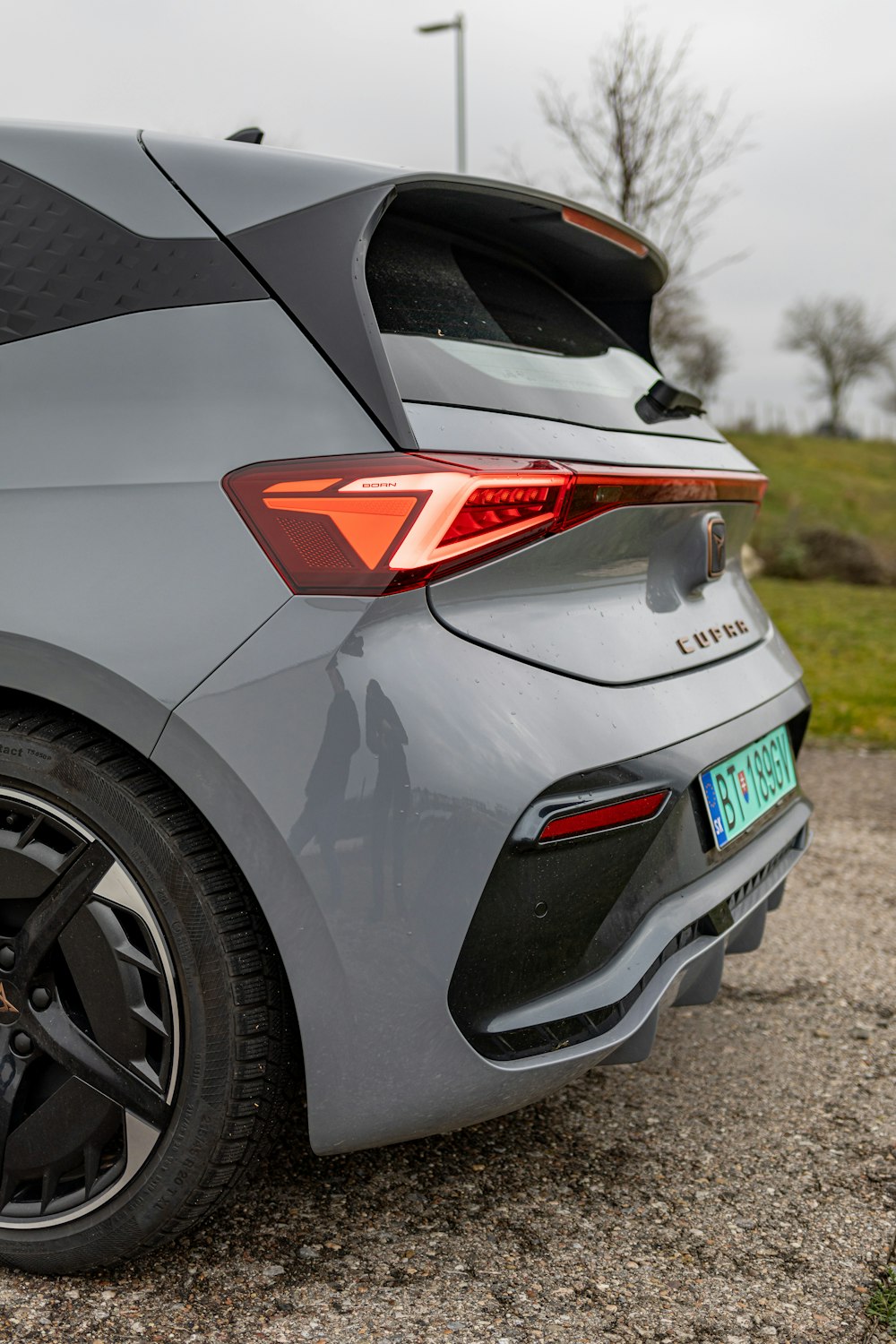 the rear end of a grey car parked on a gravel road