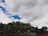 A rugged collection of rocks and boulders is set against a backdrop of a partly cloudy sky. The rocks are irregularly shaped and covered in patches of vegetation, giving a natural and untouched appearance.