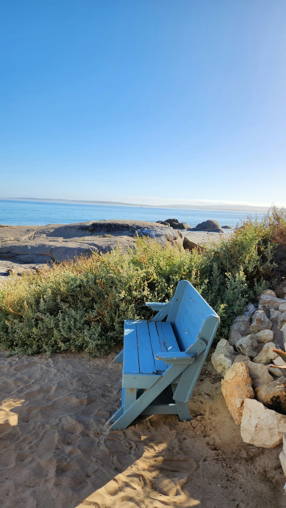 um banco azul sentado em cima de uma praia de areia